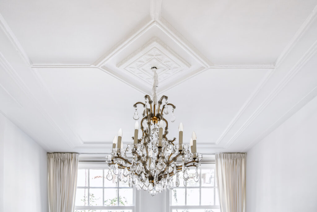 Klassiek ornamentenplafond met een vierkante sierlijst en kristallen kroonluchter.