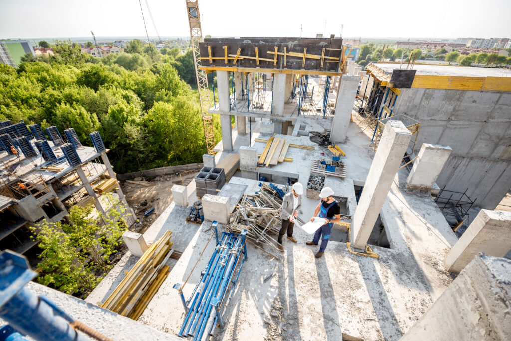 Constructiesite met bouwvakkers en ingenieurs van een bouwbedrijf in Amsterdam die plannen bespreken tussen betonconstructies en bouwmaterialen.